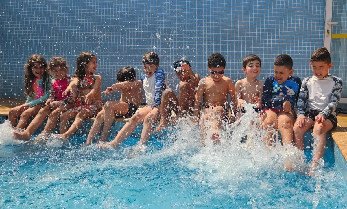 Crianças sentadas na borda da piscina do Colégio Salgueiro batendo os pés na água