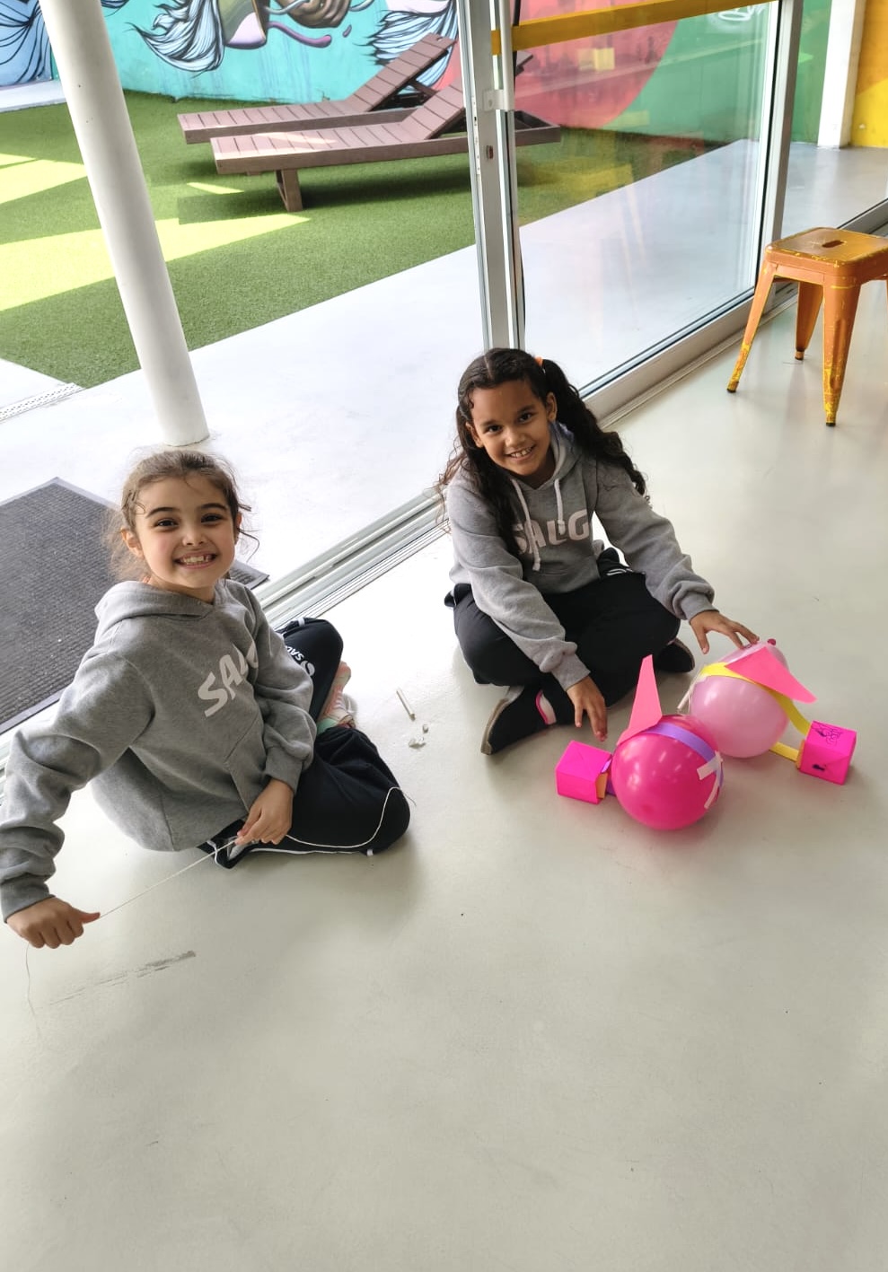 Duas meninas sorrindo ao lado de seus foguetes de bexiga rosa na atividade de Cultura e Inovação — aula de Cultura e Inovação, Colégio Salgueiro em Interlagos