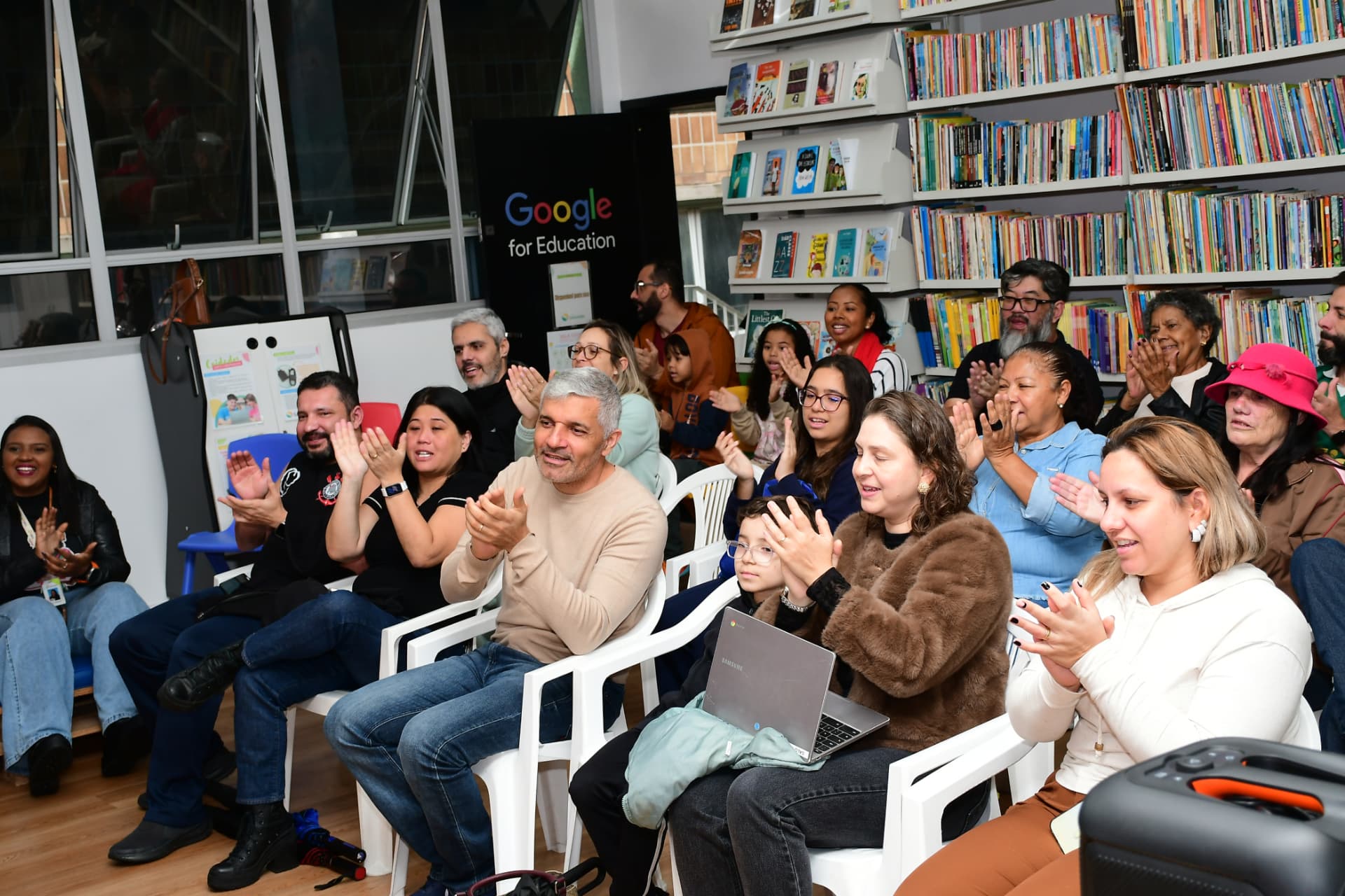 Famílias aplaudindo a apresentação dos projetos solidários na biblioteca
