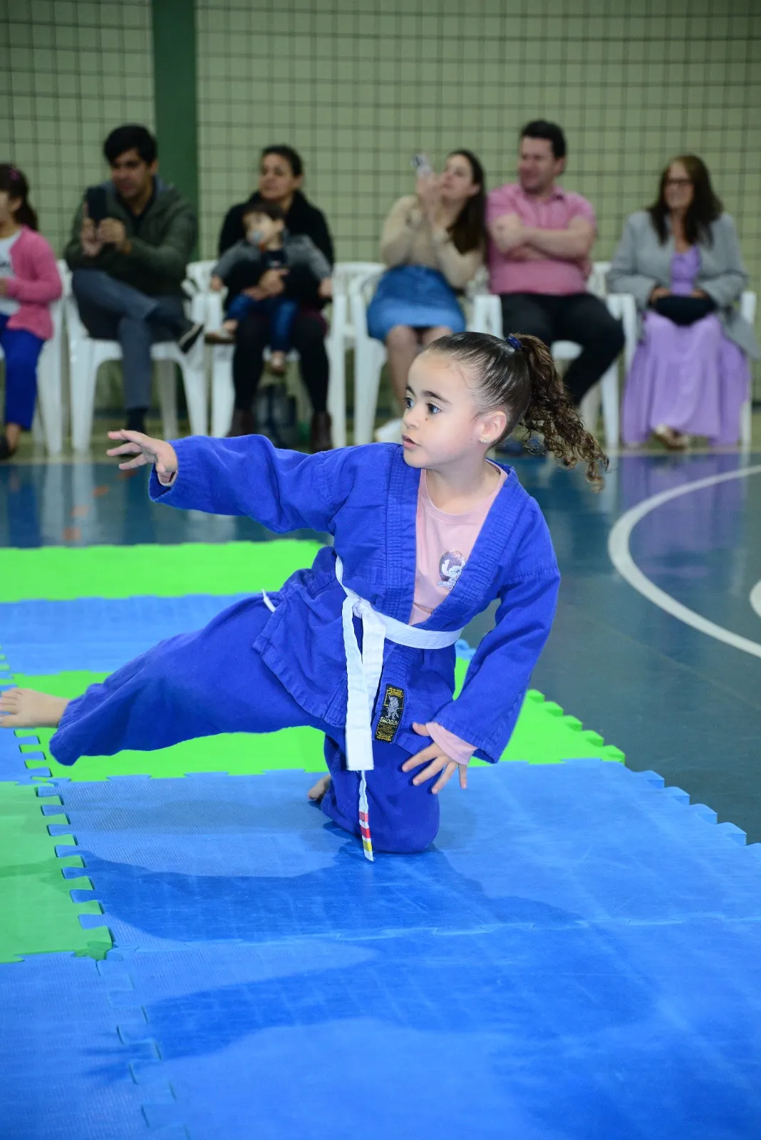 Aluna de quimono azul faz movimento de judô no tatame diante das famílias — Troca de Faixa de Judô, Colégio Salgueiro em Interlagos